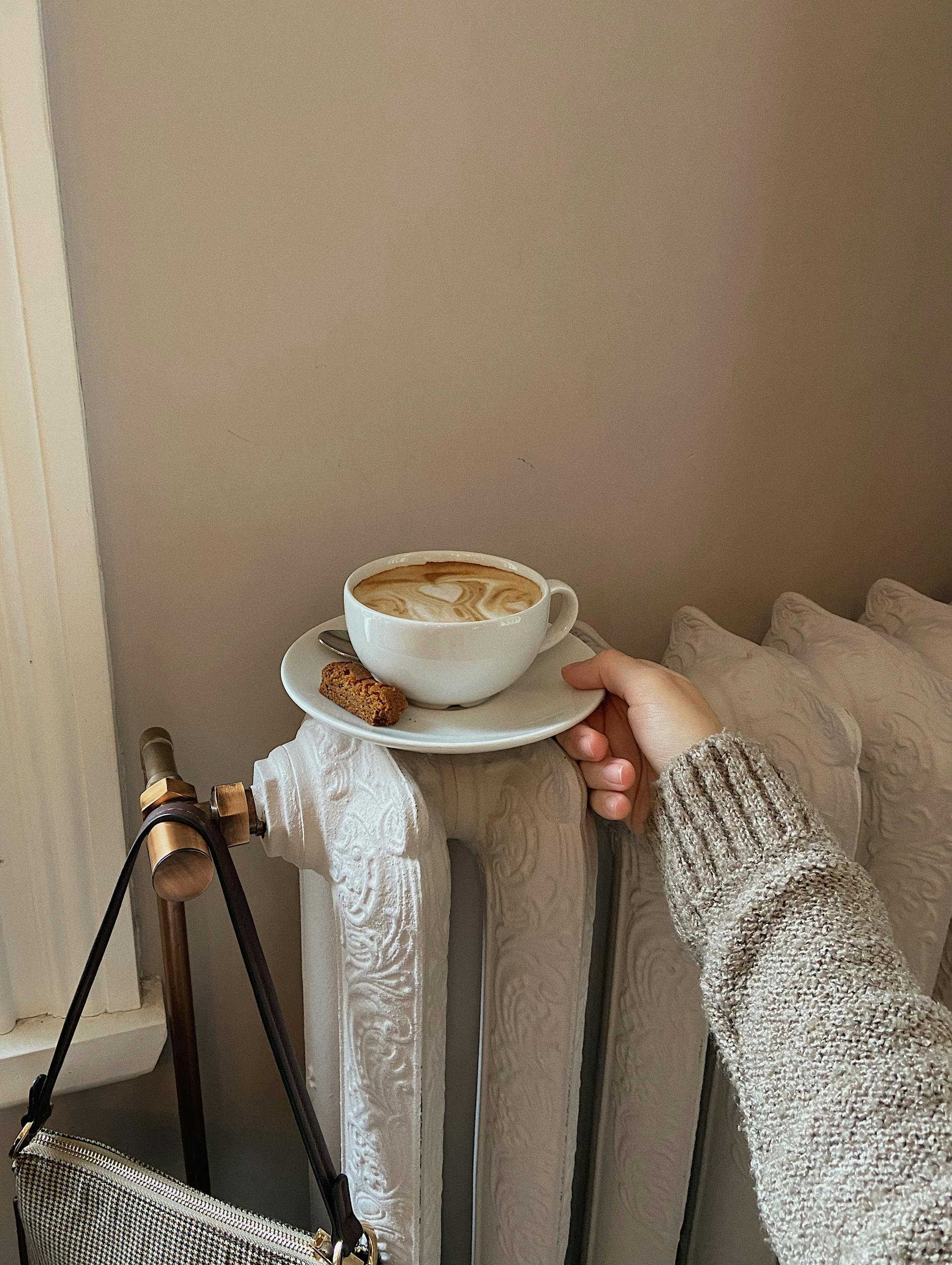 A hand holds a coffee cup atop a vintage heater, creating a warm cozy scene indoors.