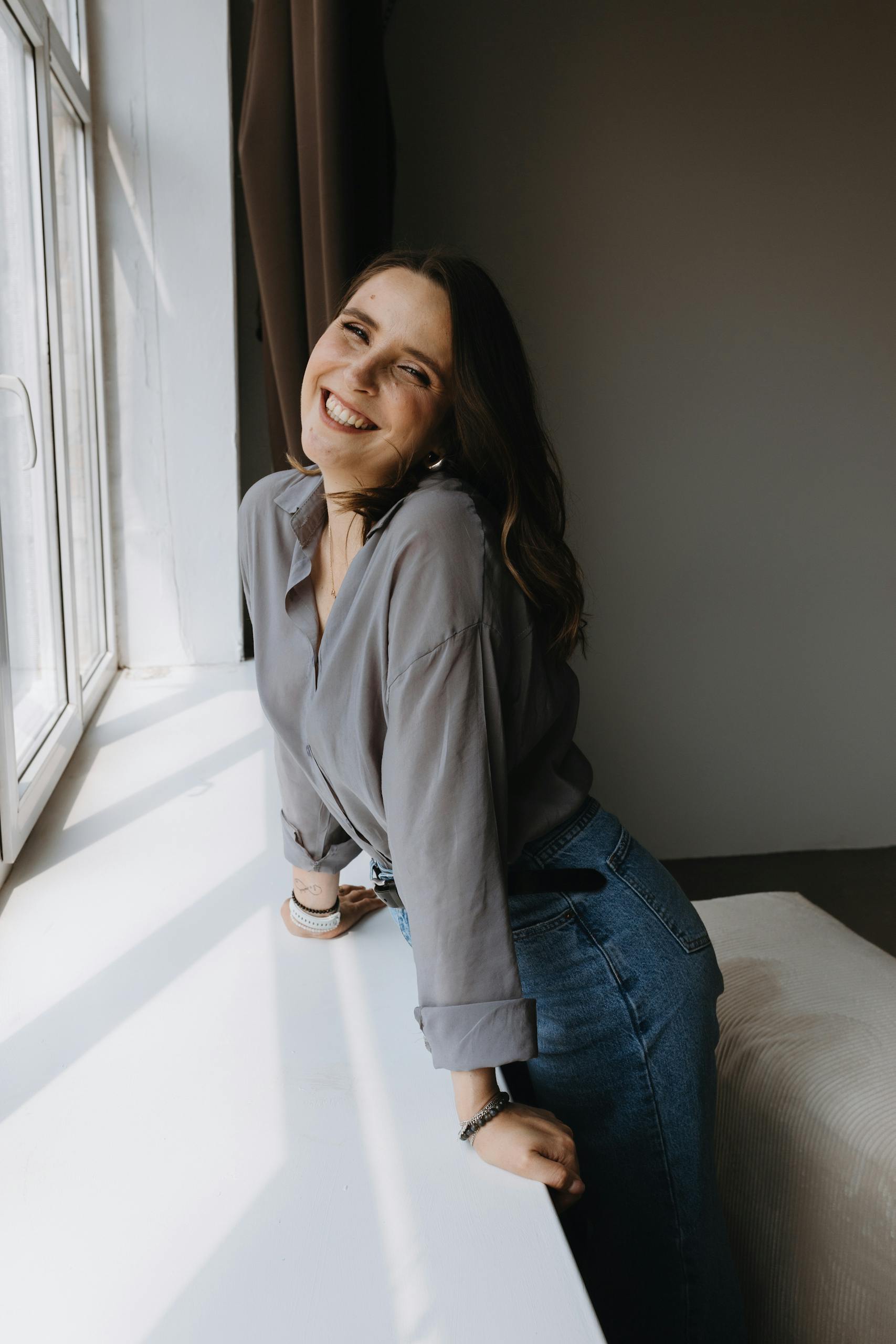 Happy woman leaning by window, enjoying sunlight indoors.
